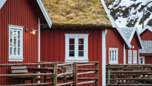 Maison en bois scandinave rouge avec des menuiseries blanches et un toit de chaume