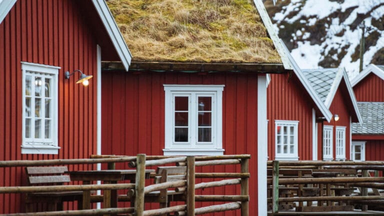 Maison en bois scandinave rouge avec des menuiseries blanches et un toit de chaume